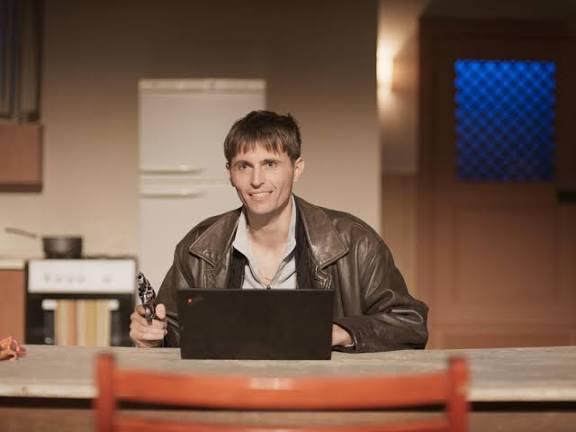 le personnage face au public avec un PC et un flingue